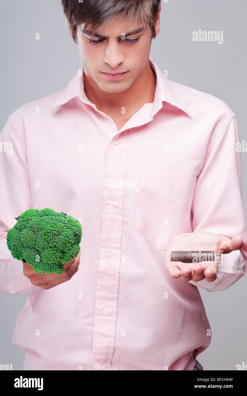 L'uomo scegliendo tra i broccoli e cioccolata Foto Stock
