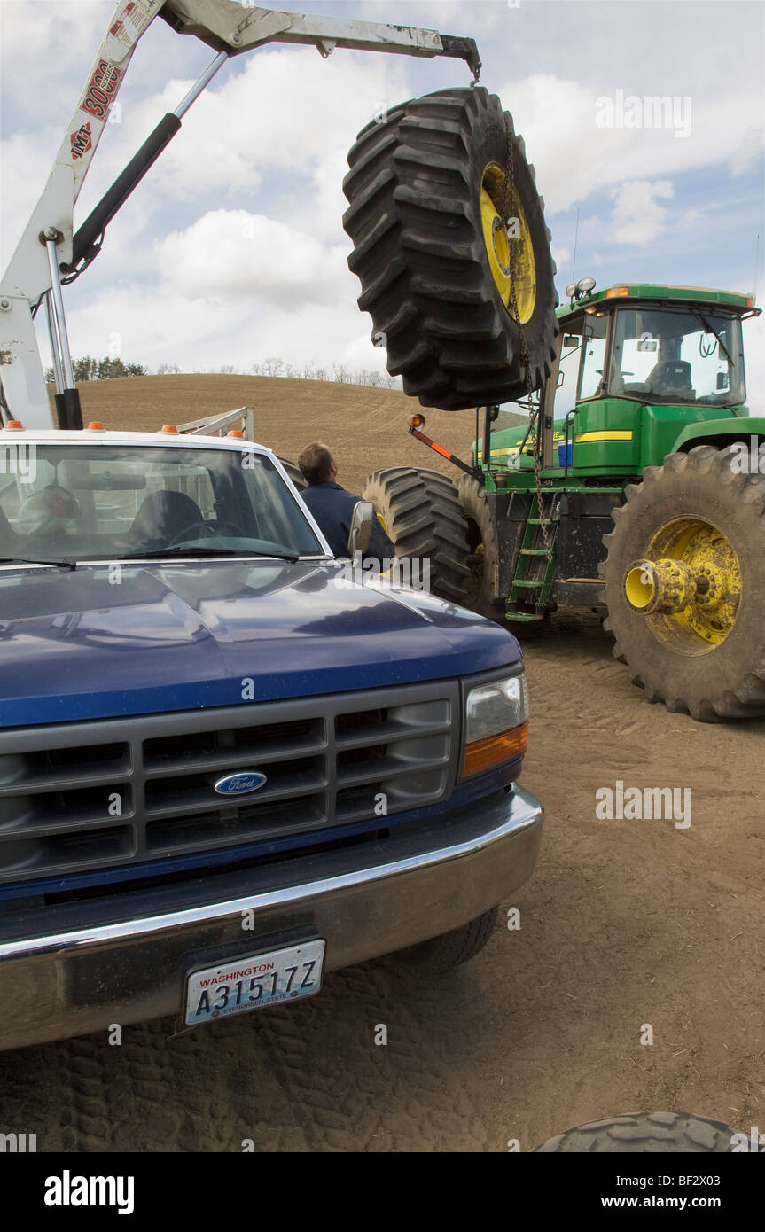 Un pneumatico tecnico lavora per cambiare il pneumatico del trattore nel campo durante la stagione della semina / Pullman, Regione Palouse, Washington, Stati Uniti d'America. Foto Stock