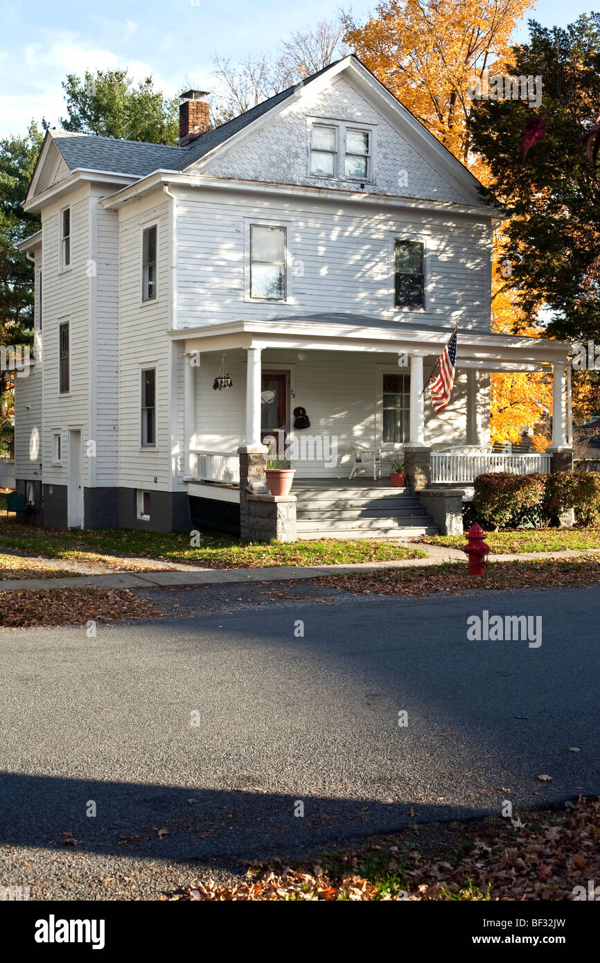 Imponente dipinto di bianco clapboard house incorniciato dalla chioma fiammeggiante & con spazioso portico anteriore battenti bandiera americana Montgomery NY Foto Stock