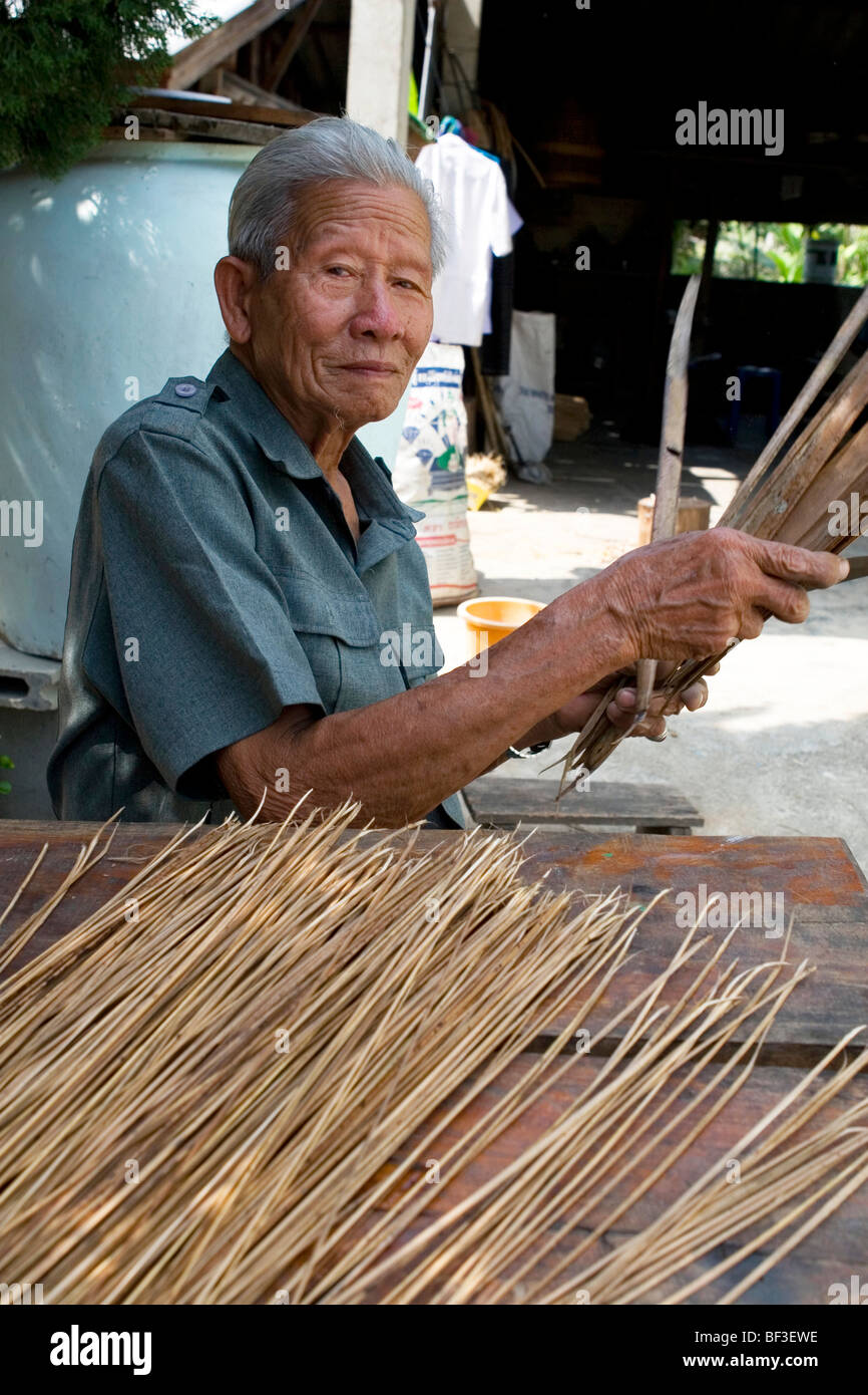 Il vecchio uomo tailandese tradizionale rendendo scope di lamelle di erba nella provincia di Chiang Rai, la Thailandia del Nord. Foto Stock