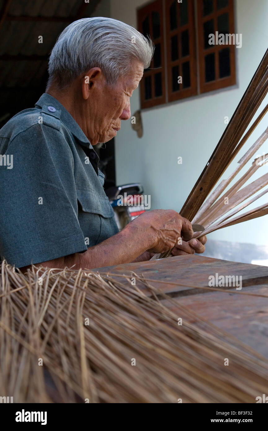 Il vecchio uomo tailandese tradizionale rendendo scope di lamelle di erba nella provincia di Chiang Rai, la Thailandia del Nord. Foto Stock