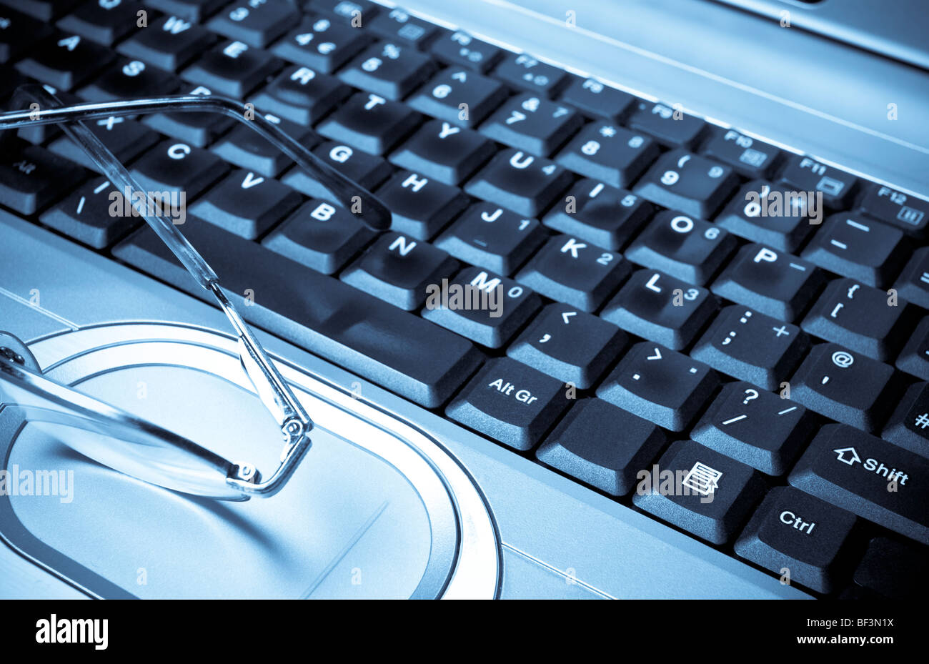 Nei toni del blu immagine monocromatica di occhiali e portatile con tastiera shallow focus sul grezzo di lavorazione per chiave Foto Stock