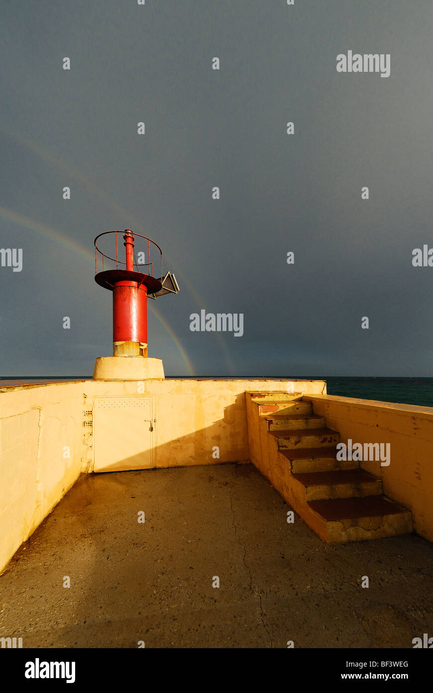 Faro rosso sul molo del piccolo porto nella parte anteriore di nuvole e arcobaleno nel Cap Negret, Altea, Costa Blanca, Spagna Foto Stock