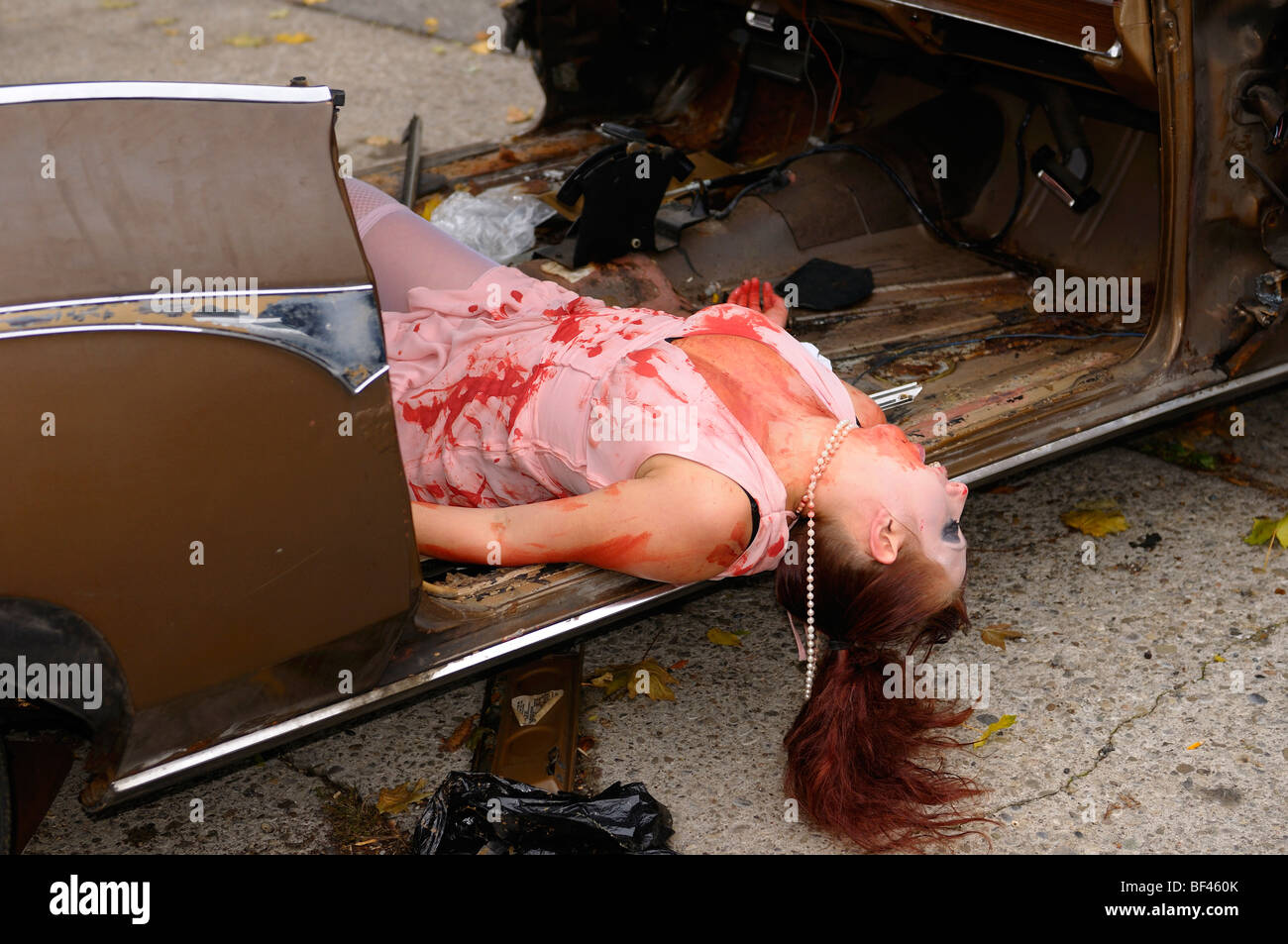 Coperti di sangue femmina in abito da sera costume dispiegata su un junked Buick Riviera Auto play deliberando a Toronto Zombie a piedi Foto Stock