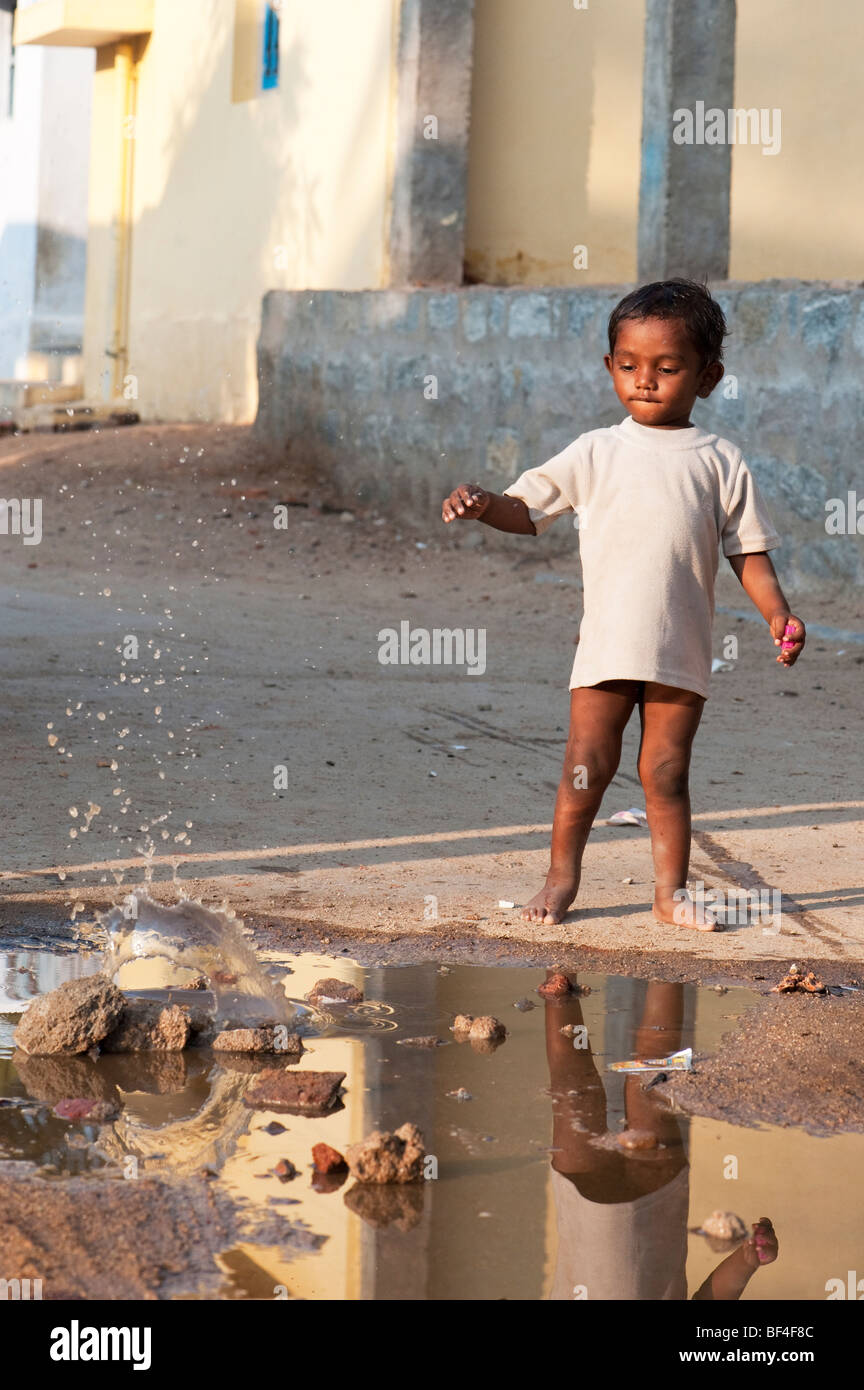 Piccolo ragazzo indiano gettando una pietra in una pozza d'acqua in un Indiano street. Puttaparthi, Andhra Pradesh, India Foto Stock