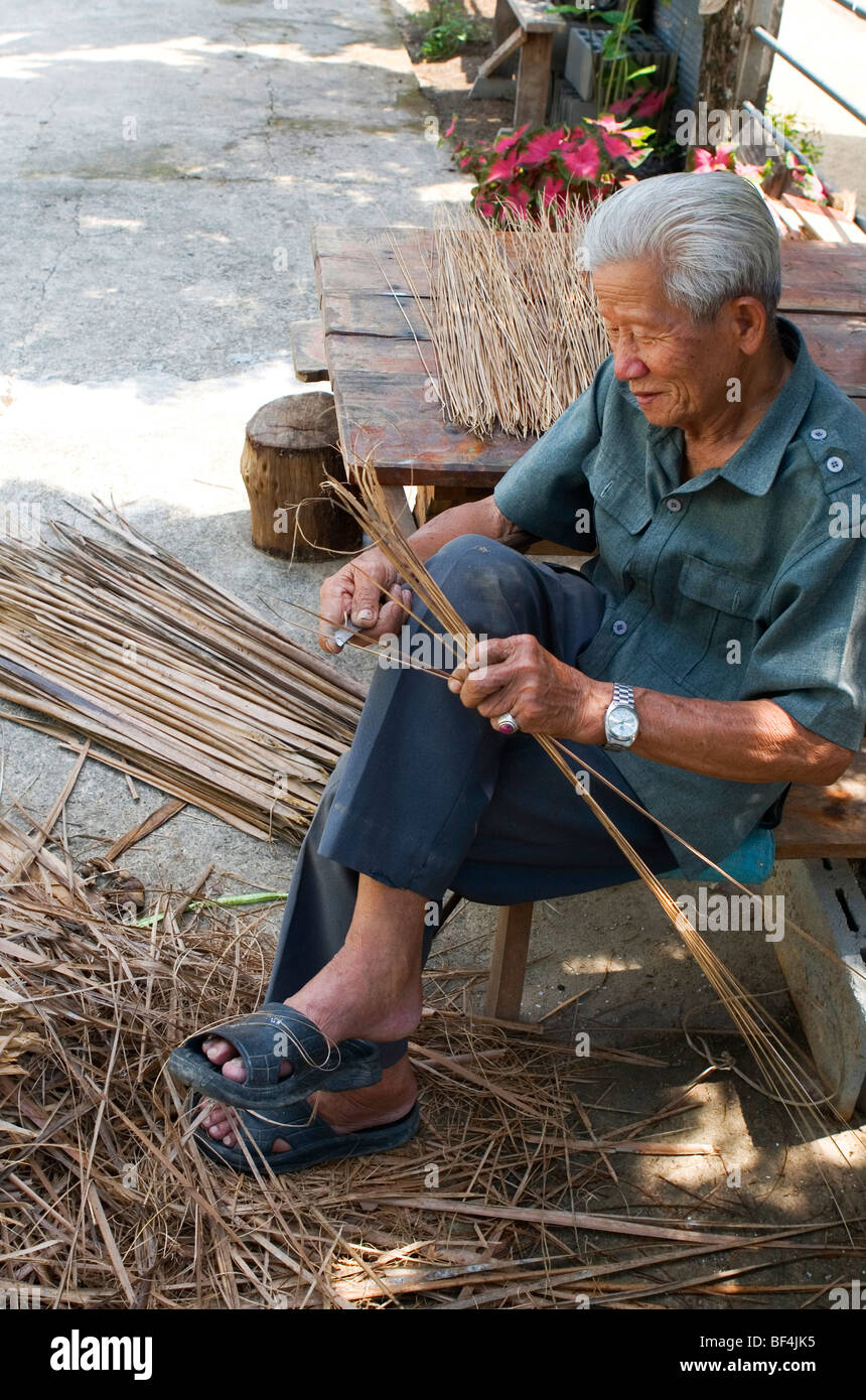 Il vecchio uomo tailandese tradizionale rendendo scope di lamelle di erba nella provincia di Chiang Rai, la Thailandia del Nord. Foto Stock