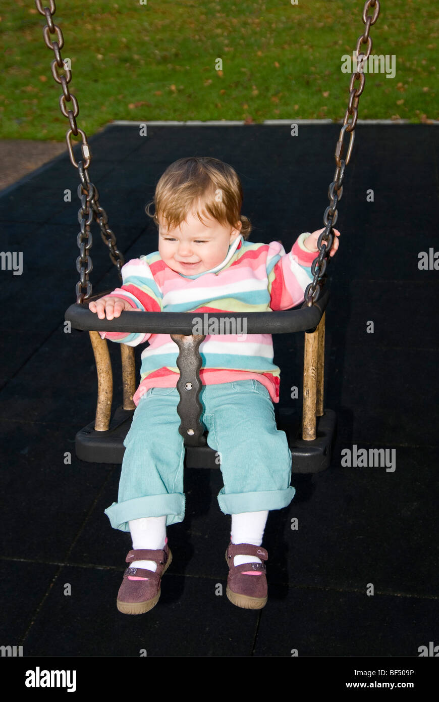 Chiudere verticale su ritratto di una piccola ragazza sorridente e avente un grande divertimento seduto su un altalena al parco. Foto Stock