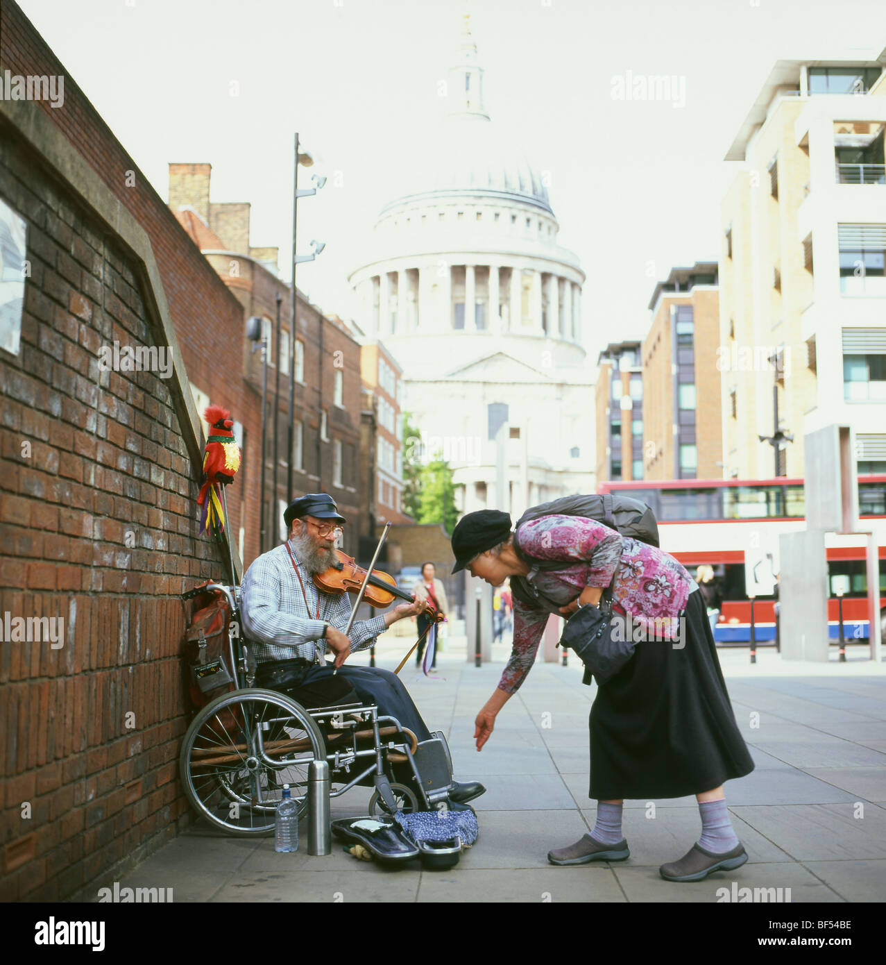 Una donna di dare i soldi per la carità di un suonatore ambulante a suonare il violino seduto in una sedia a rotelle vicino alla Cattedrale di San Paolo a Londra KATHY DEWITT Foto Stock