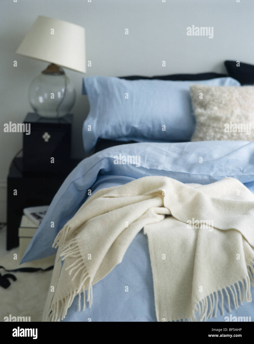 Camera da letto con vetro lampada sul comodino accanto al letto con lenzuola blu e crema di buttare la lana Foto Stock