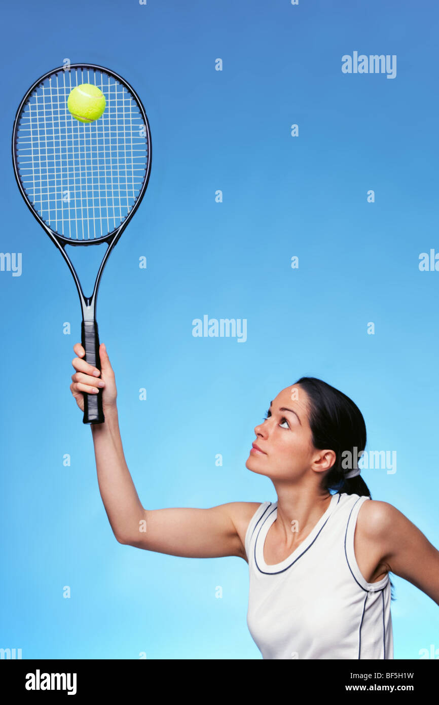 Una donna giocatore di tennis che serve contro uno sfondo blu. Foto Stock
