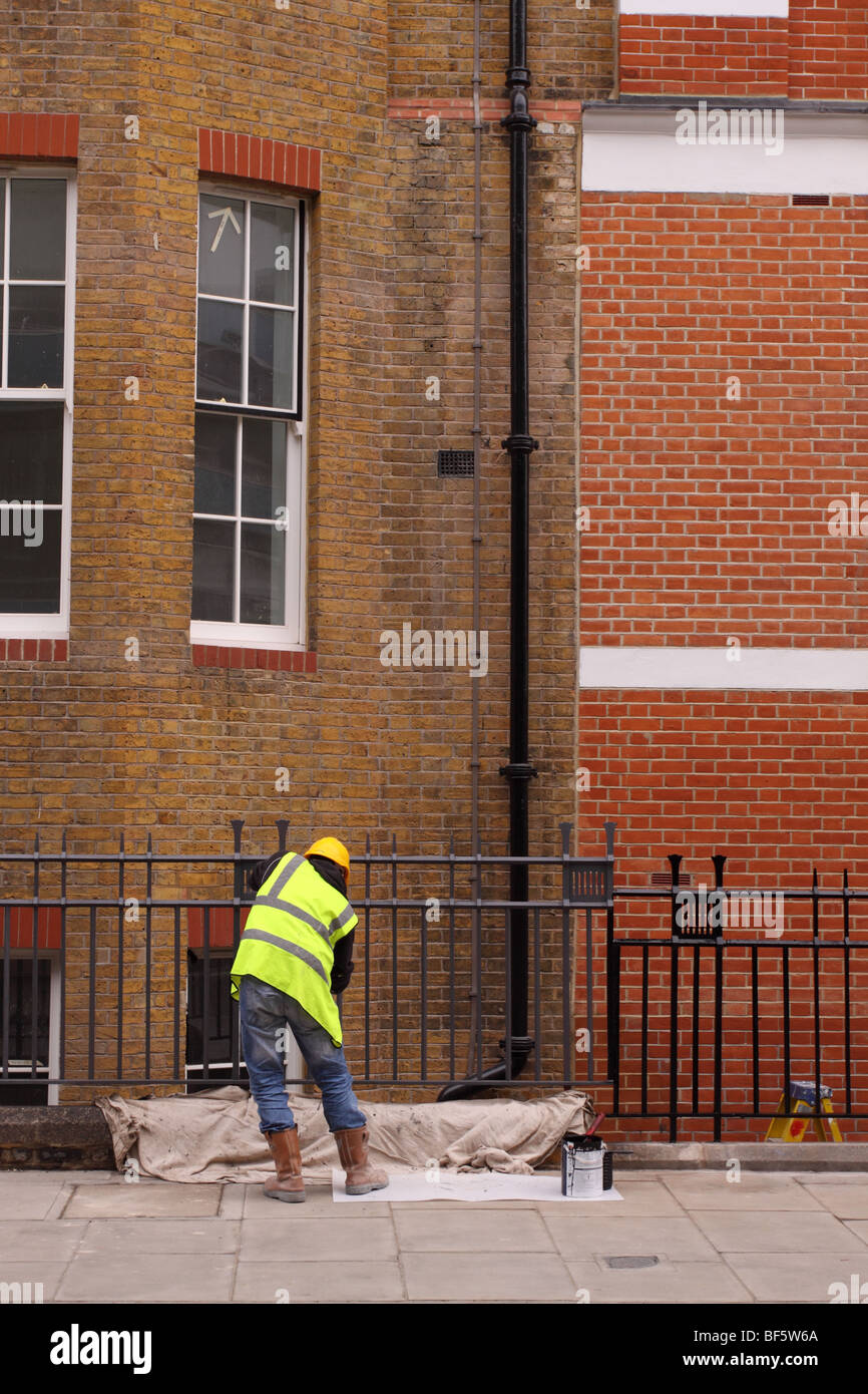 Builder lavoratore maintence uomo pittura ringhiera in ferro al di fuori di Londra blocchi di appartamenti indossando alta viz giacca casco di sicurezza Foto Stock
