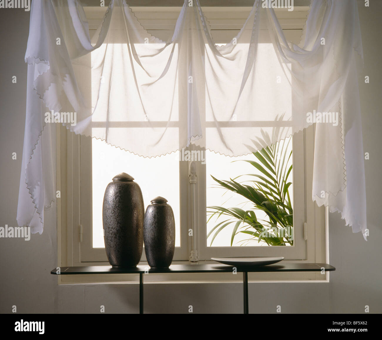 Close-up di voile bianco drappeggi su finestra sopra tavolo console con vasi di nero Foto Stock
