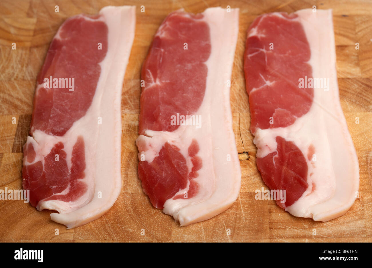 Tre strisce di materie back bacon dal british organico a doppio spiovente suini allevati in Irlanda steso su una tavola di legno macellai di blocco Foto Stock