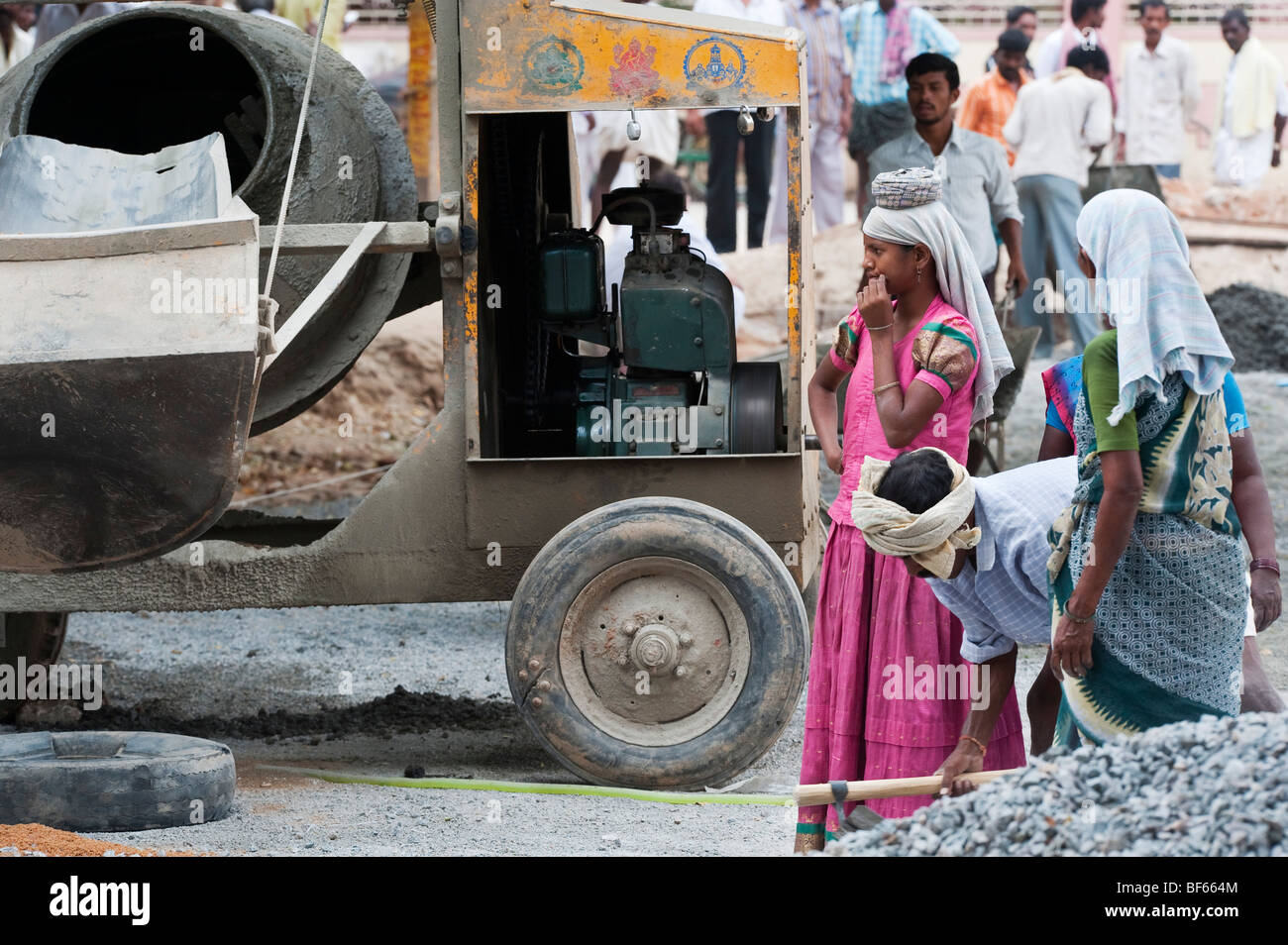 Le donne indiane in piedi accanto a una grande betoniera mentre lavorano sulle strade in Puttaparthi, Andhra Pradesh, India. Foto Stock