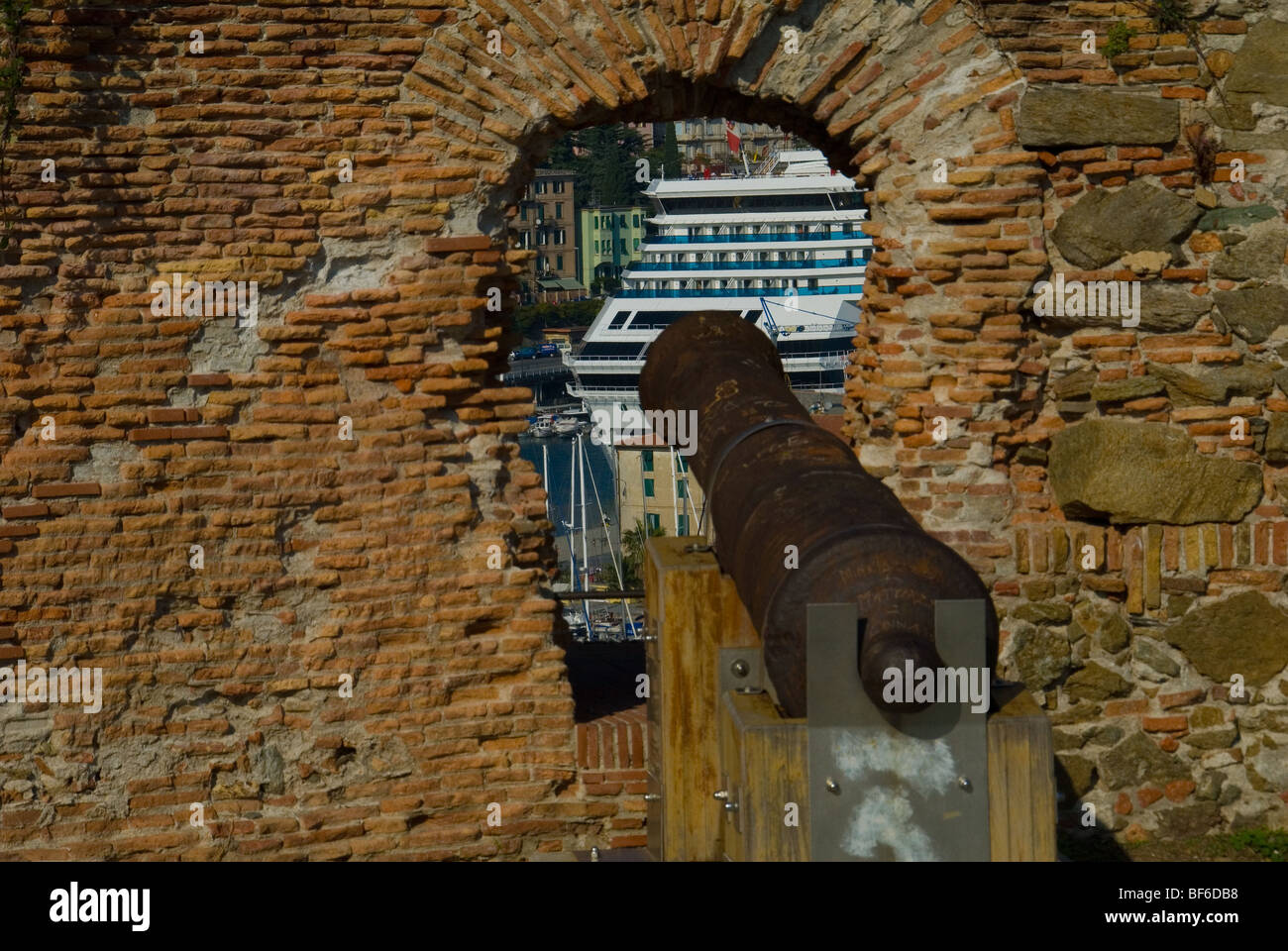 Un vecchio cannone sporgente da un oblò e puntando verso una moderna nave da crociera in un antico Savona fortezza nel Nord Italia Foto Stock