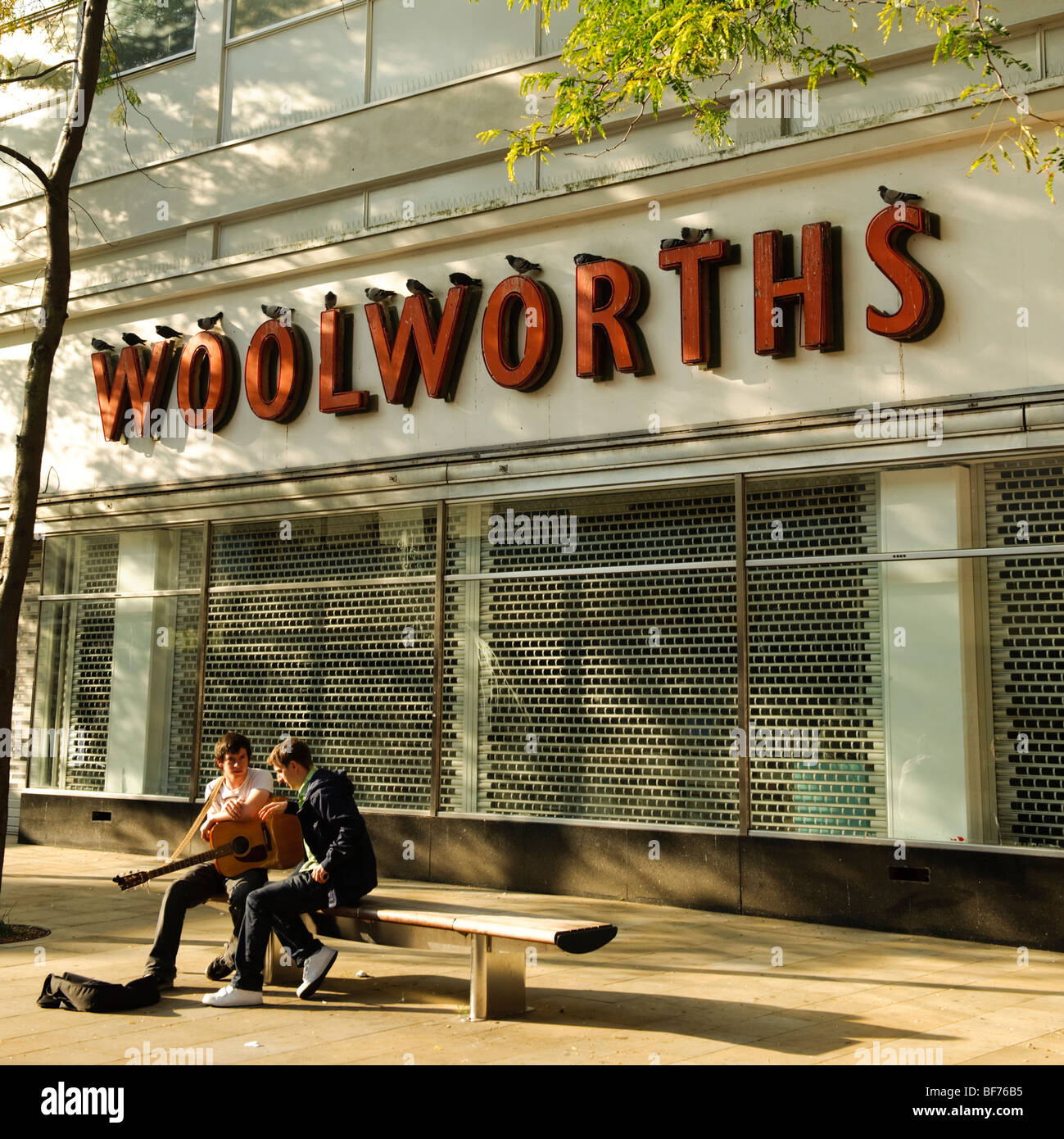 Due giovani seduta su una panchina al di fuori di un chiuso il ramo di woolworths store centro di Swansea Wales UK Foto Stock