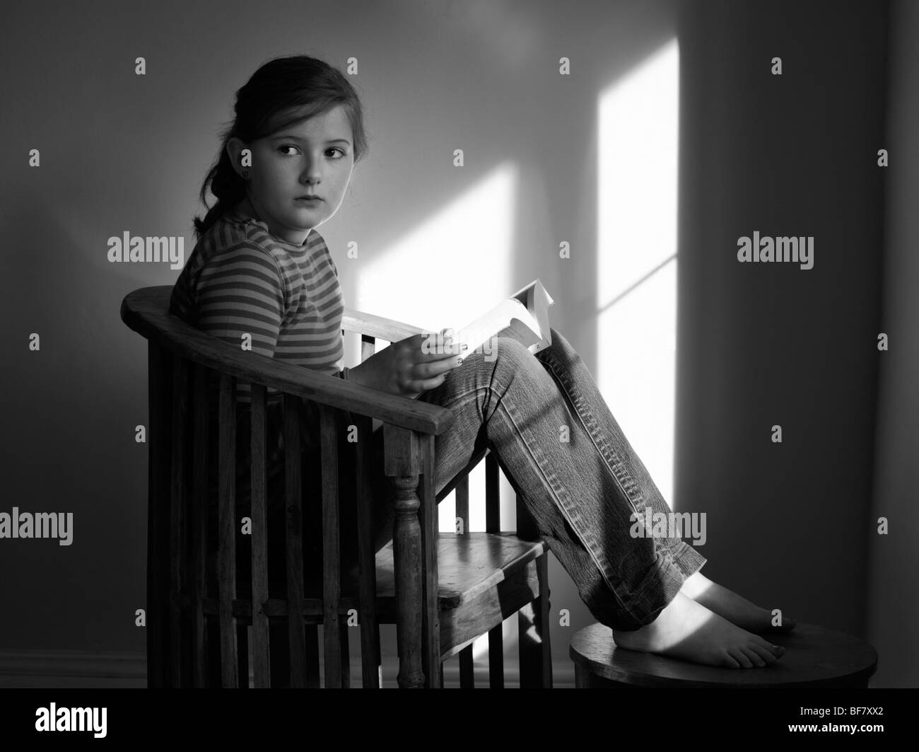 Dieci anni di vecchia ragazza guardando dalla lettura di un libro dalla luce proveniente da una finestra. Foto Stock