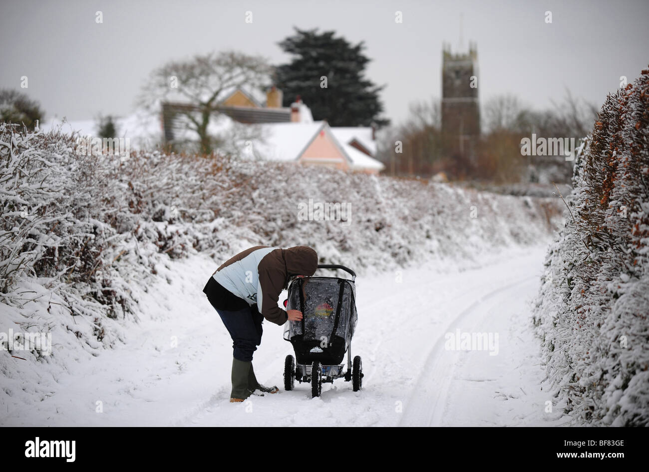 Una madre a piedi una baby lungo una strada di campagna nella neve in alta Bickington, Devon Foto Stock