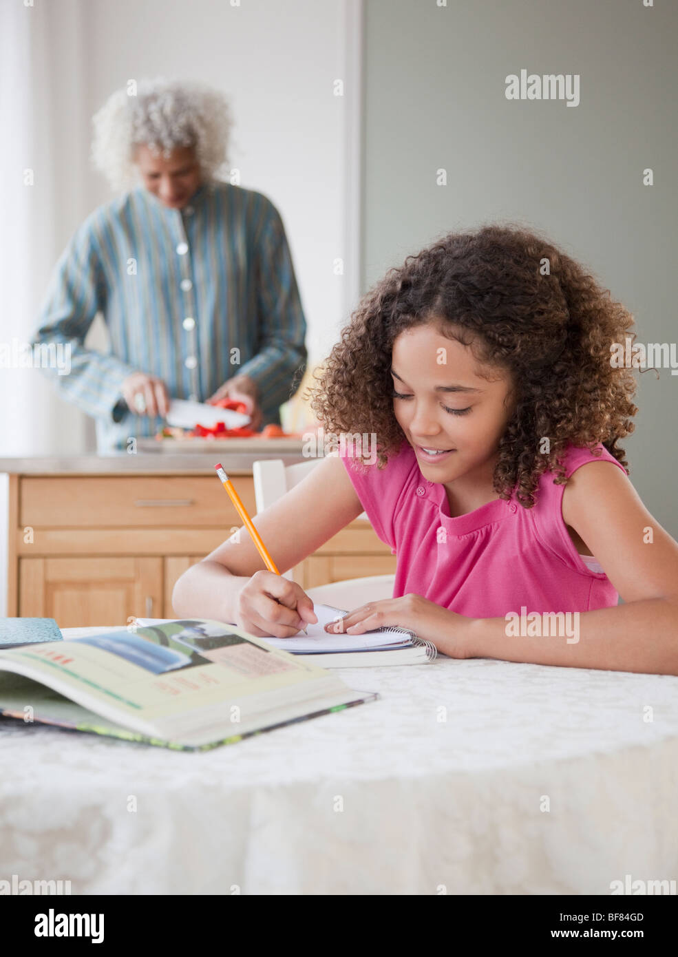 Ragazza facendo compiti a casa con la nonna in background Foto Stock