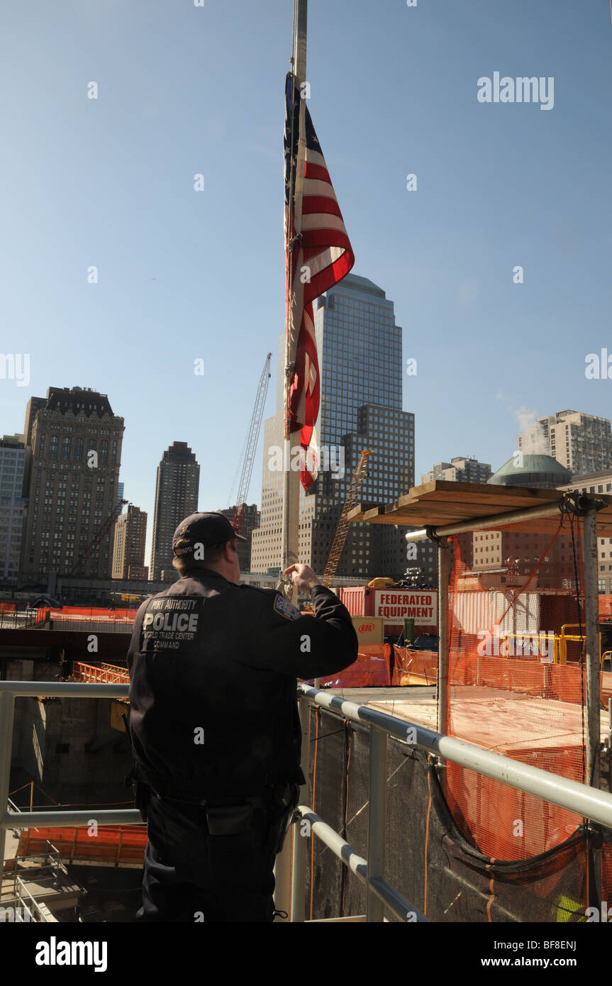 Un Autorità Portuale poliziotto abbassa la bandiera degli Stati Uniti al montante di metà presso il World Trade Centre in un cantiere in Lower Manhattan. Foto Stock