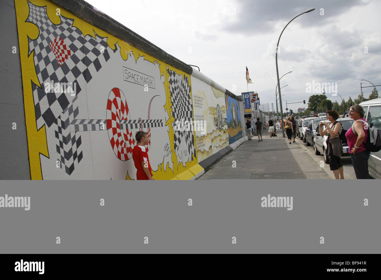 Un giovane turista in posa per una foto con il muro di Berlino, la East Side Gallery, a 1.3km-lungo la sezione della parete vicino al centro di B Foto Stock