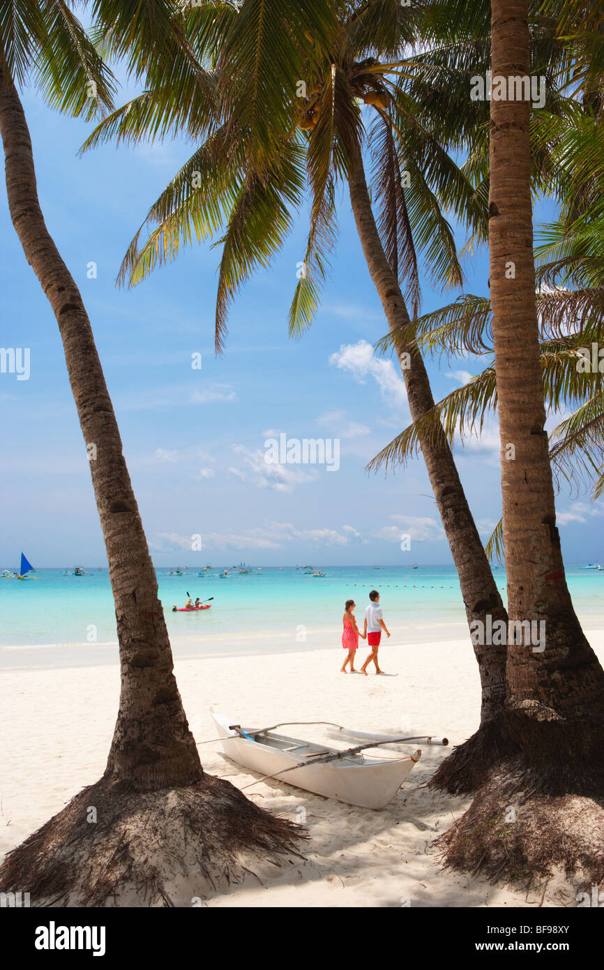 Barca bianca tra due palme e giovane walkng lungo la spiaggia Boracay; Il Visayas; Filippine. Foto Stock