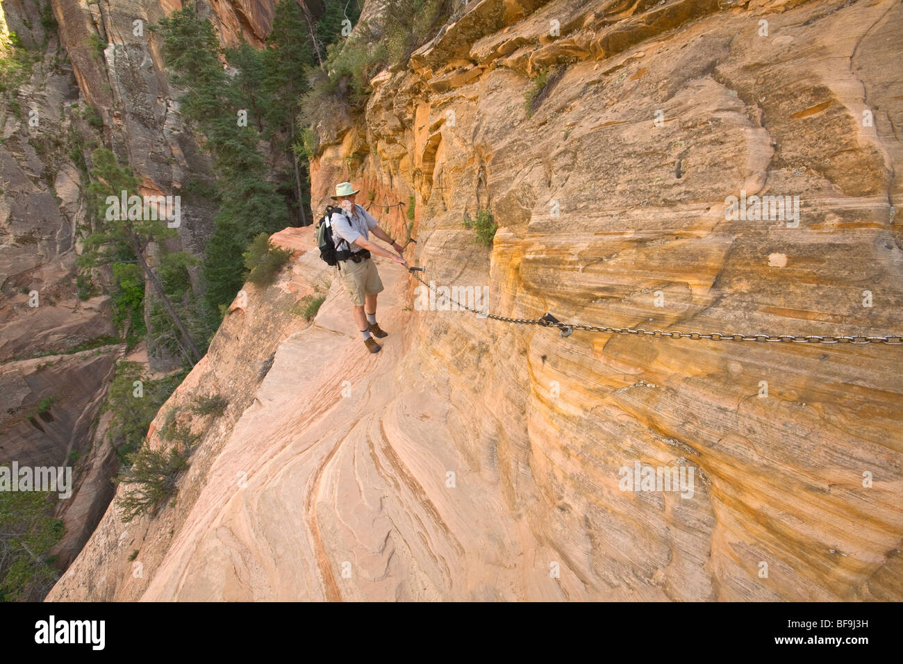Escursionista utilizzando catene di sostegno lungo la scogliera a strapiombo su Hidden Canyon Trail sopra Zion Canyon al Parco Nazionale Zion, Utah Foto Stock