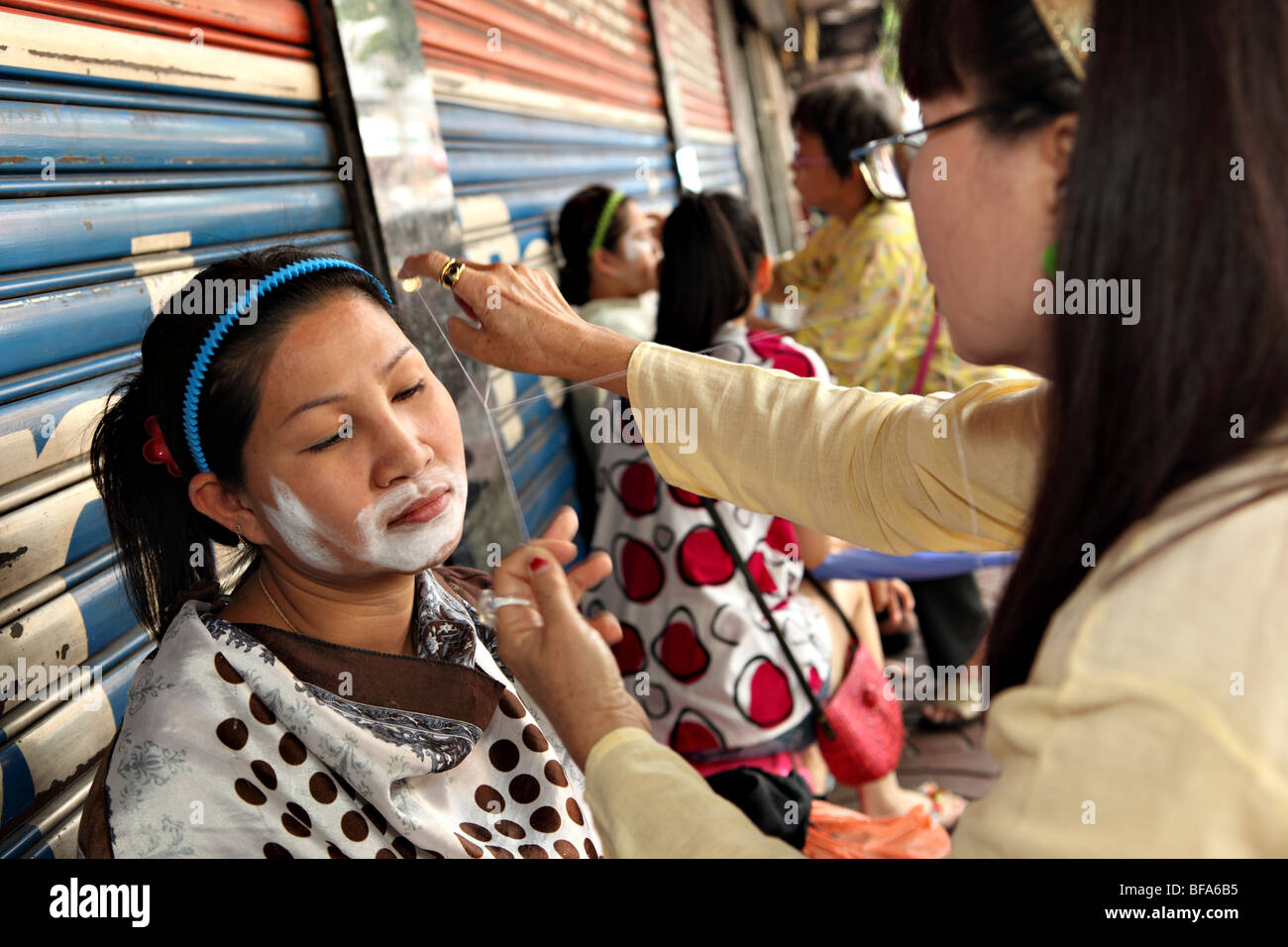 Tailandese donne ottenere i loro capelli facciali rasate sulla strada di Bangkok. Foto Stock