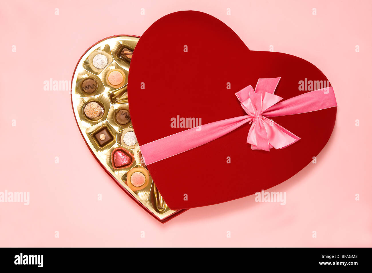 Cuore rosso a forma di scatola di cioccolatini con il nastro rosa su sfondo rosa Foto Stock
