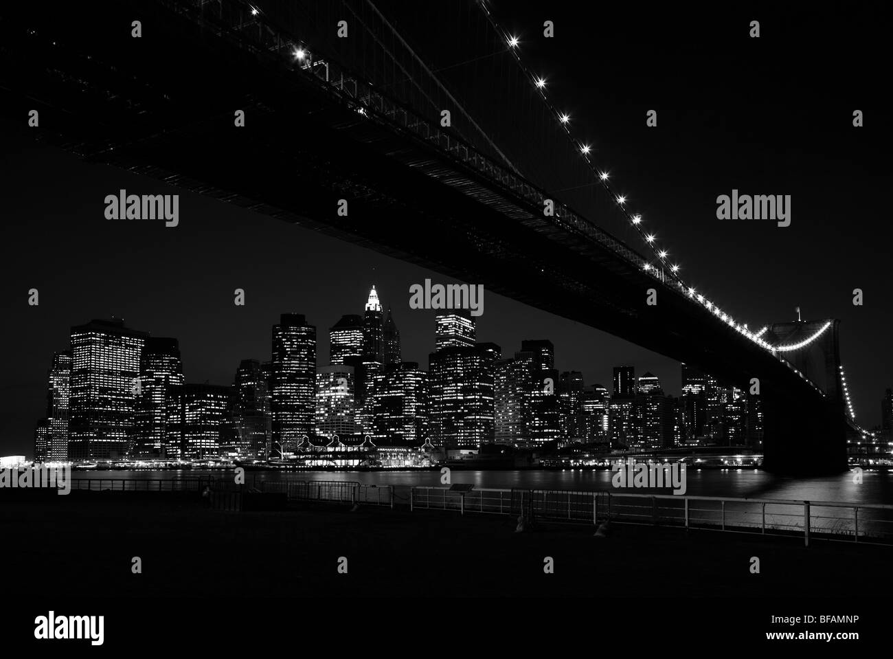 La vista da sotto il ponte di Brooklyn verso la parte inferiore di Manhattan il quartiere finanziario di New York, di notte in bianco e nero. Foto Stock