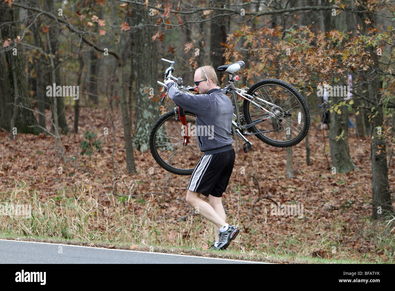 Un uomo che porta la sua bicicletta di montagna fuori del bosco. La moto è alta sulla sua spalla. Foto Stock
