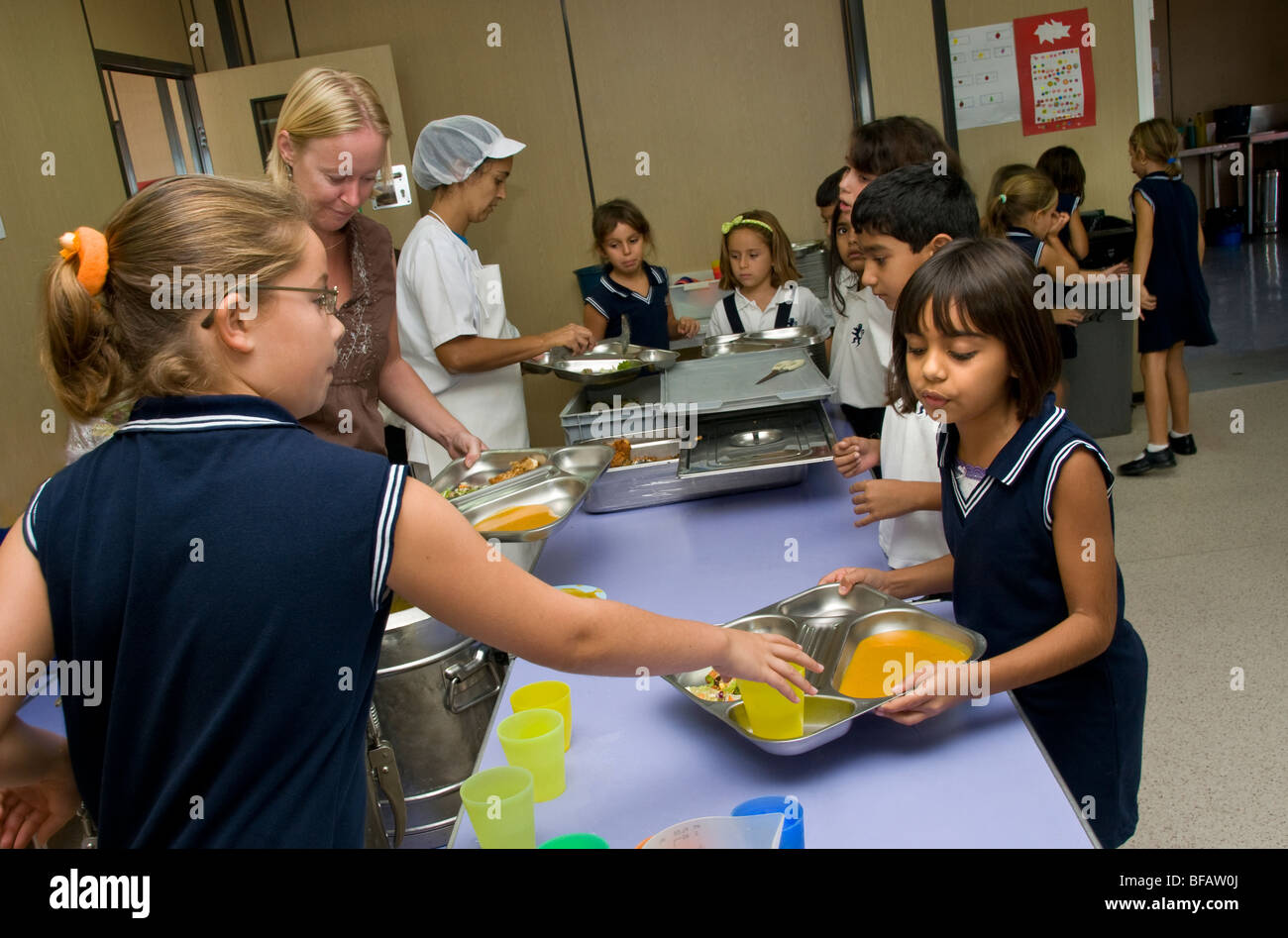 Occupato junior mensa scolastica con la ragazza di aiutare l'ora di pranzo il personale in servizio un sano pasti equilibrati Foto Stock