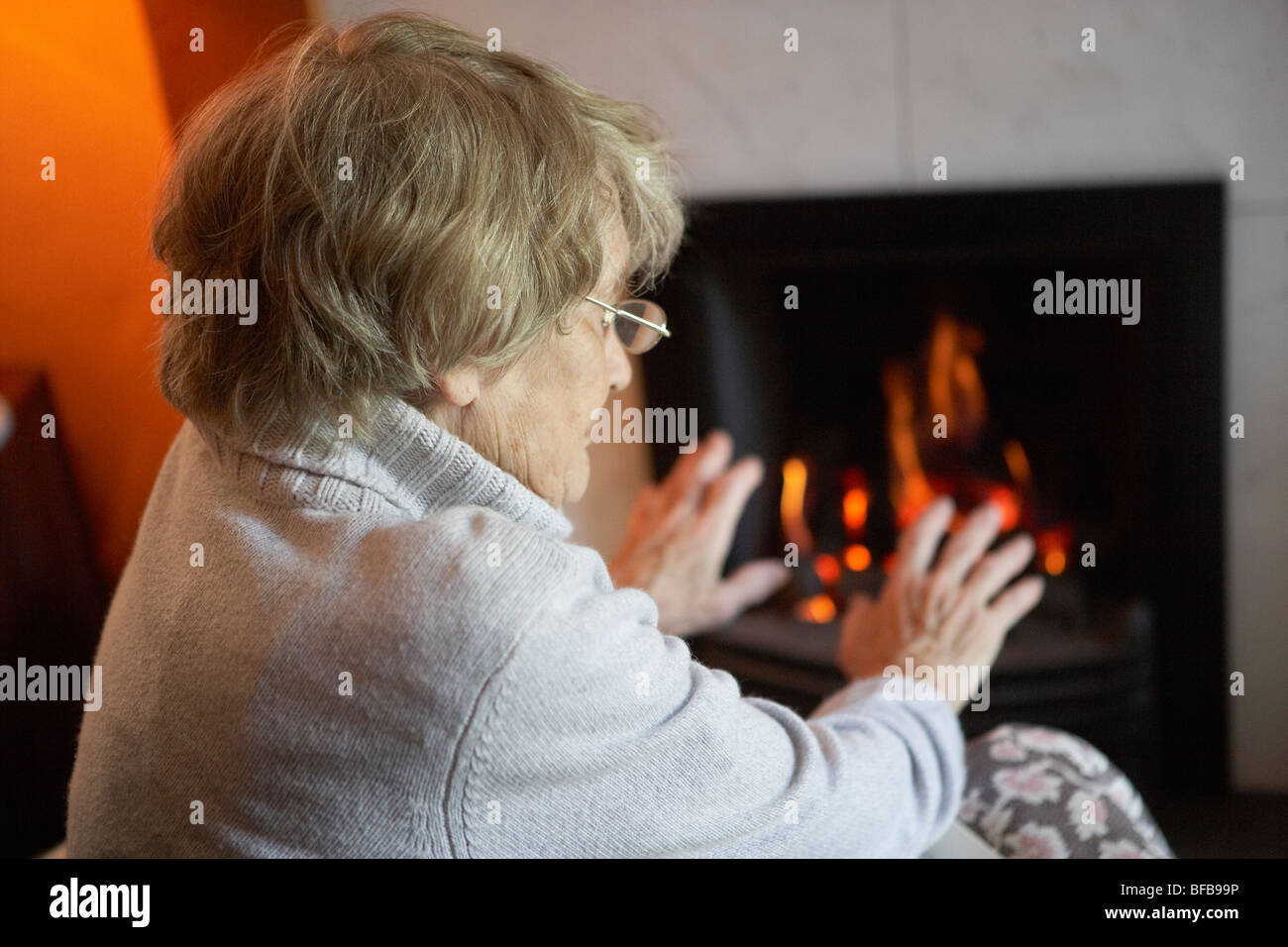 Senior donna Mani di riscaldamento da un incendio in casa Foto Stock