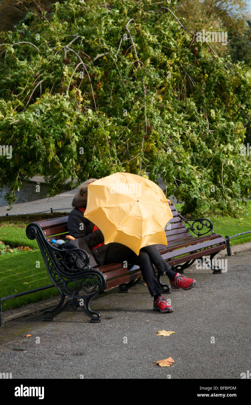 Donne ripara dal vento e dalla pioggia sotto un ombrello in stephens green Dublino Irlanda. Foto Stock