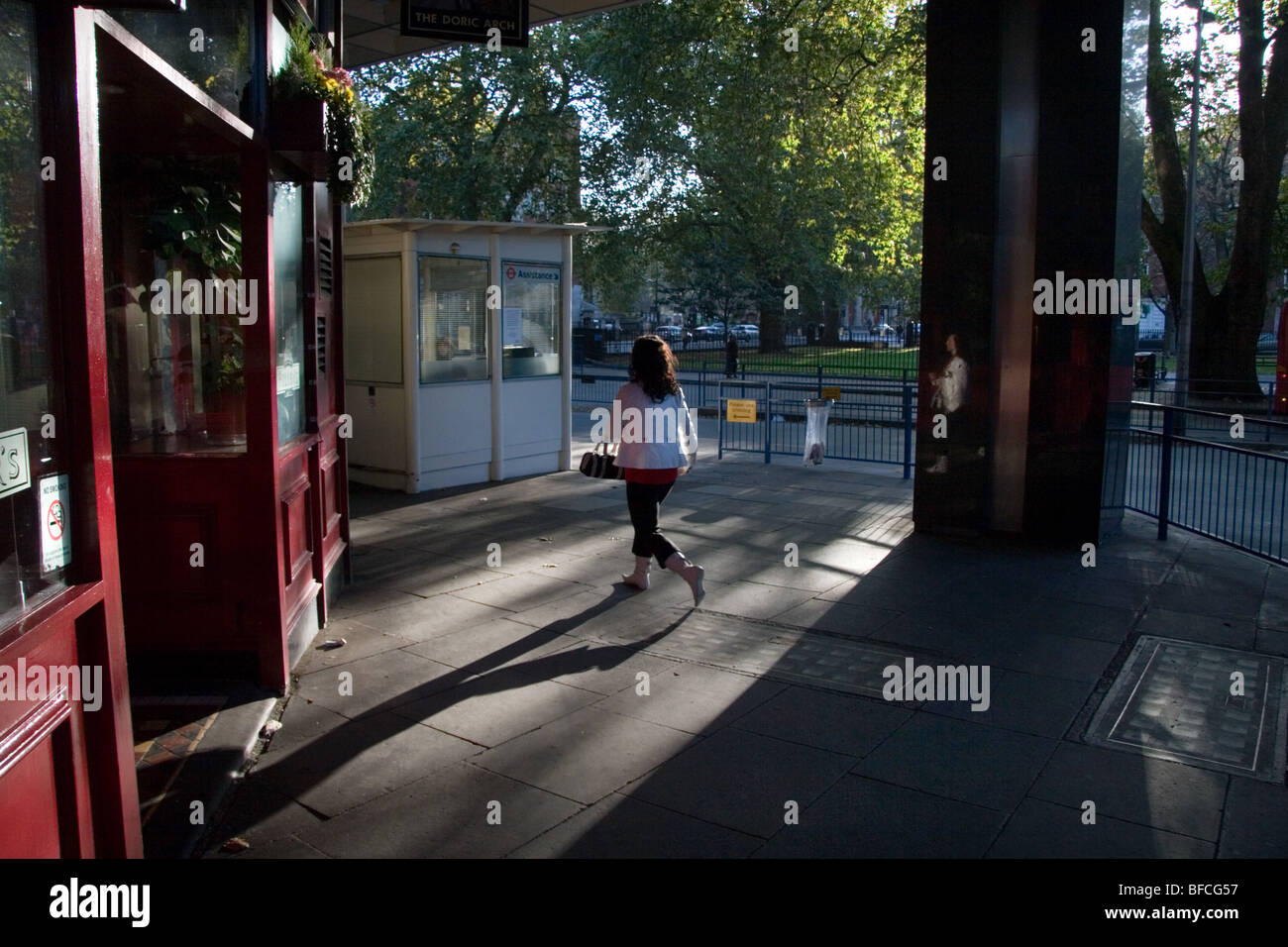 Una donna che cammina vicino la stazione di Euston, London, getta una lunga ombra e una riflessione in una pietra lucidata pilastro Foto Stock
