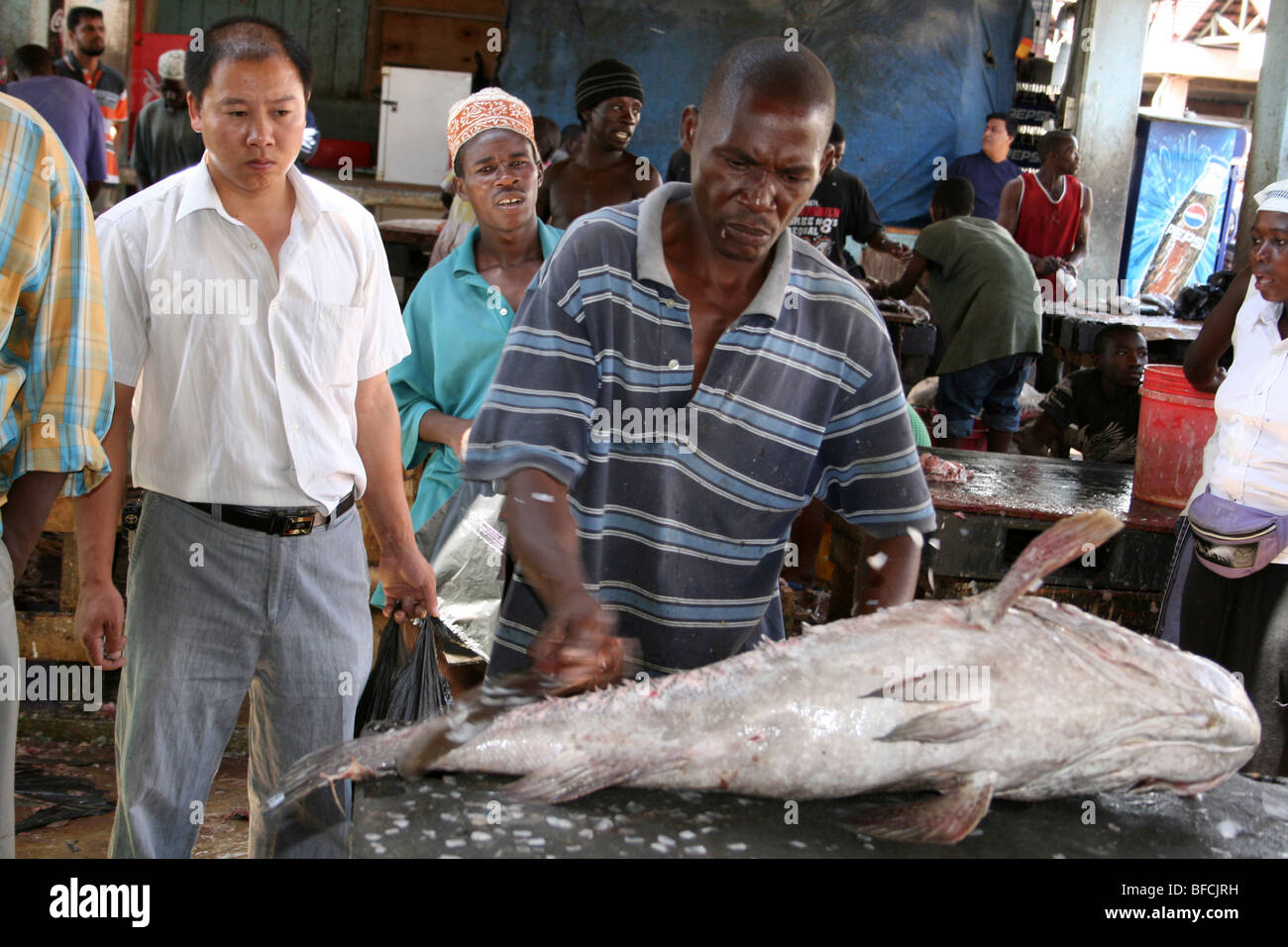 L'uomo De-scaling di pesci di grandi dimensioni a Kivukoni Mercato del Pesce, Dar-Es-Salaam, Tanzania Foto Stock