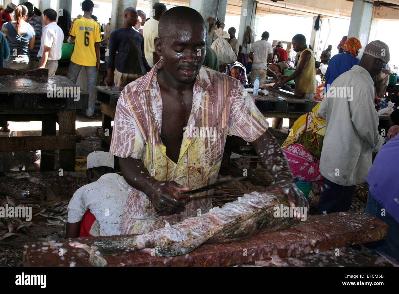 L'uomo De-scaling di pesci di grandi dimensioni a Kivukoni Mercato del Pesce, Dar-Es-Salaam, Tanzania Foto Stock