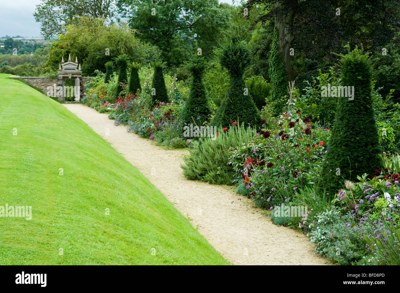 Prato e il confine di fiori punteggiato da Yew pilastri a Hanham giardini di corte, Cotswolds, REGNO UNITO Foto Stock