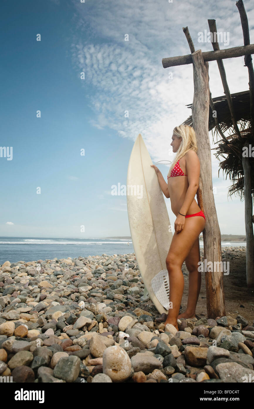 Una ragazza in piedi in un bikini rosso con una tavola da surf su una  spiaggia rocciosa accanto ad una cornice in legno capanna Foto stock - Alamy