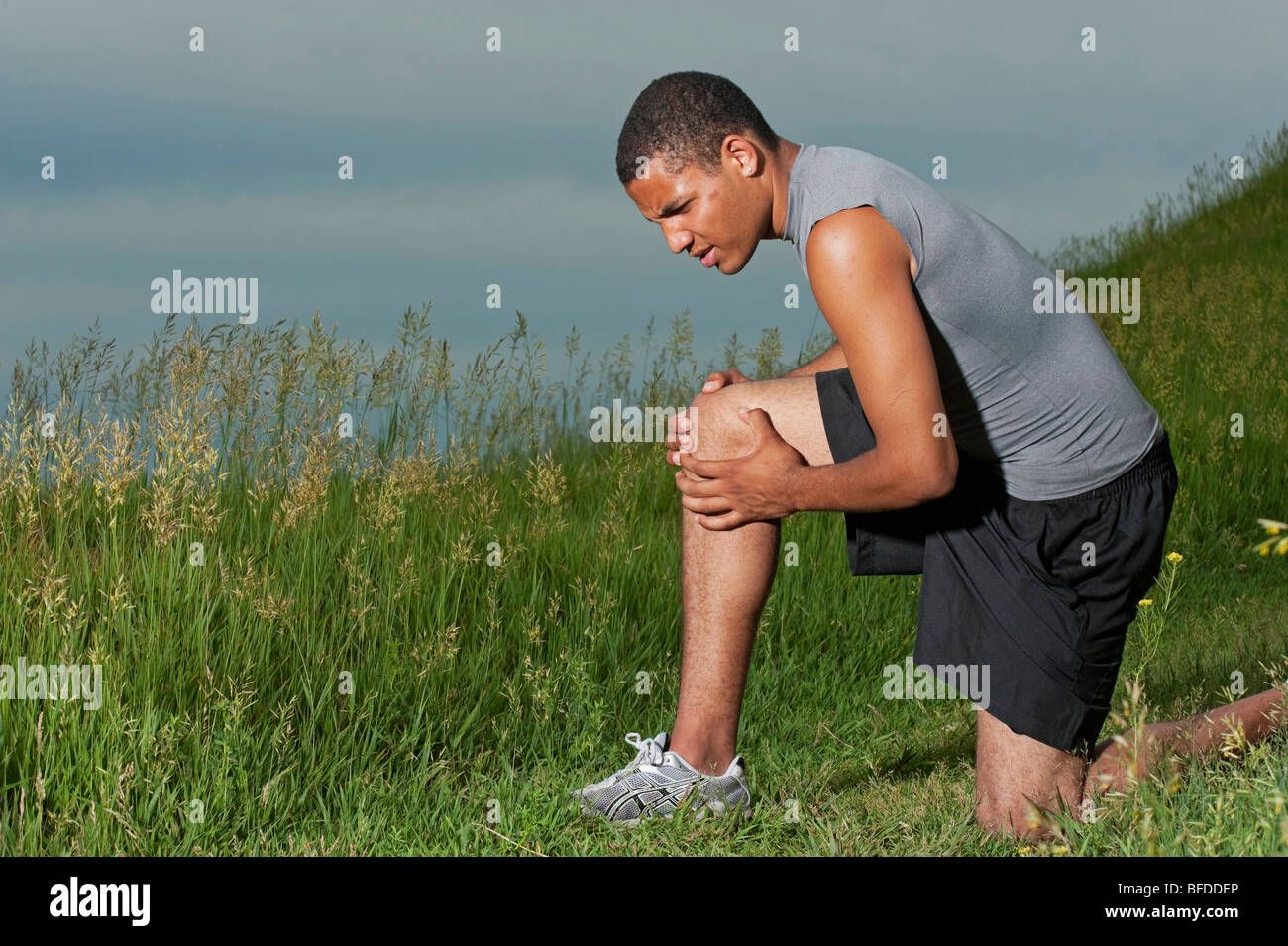 Giovane uomo detiene un ginocchio infortunato dopo aver eseguito sul sentiero di erba a Tumulo di spirito, South Dakota. Foto Stock