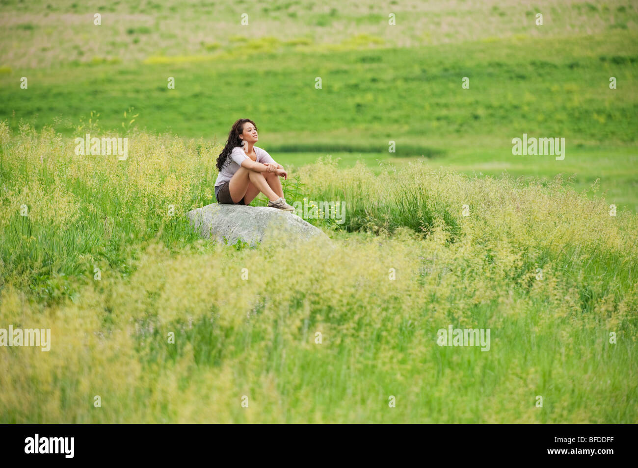 Giovane donna posa su roccia in un colore verde brillante campo in spirito Mound, South Dakota. Foto Stock