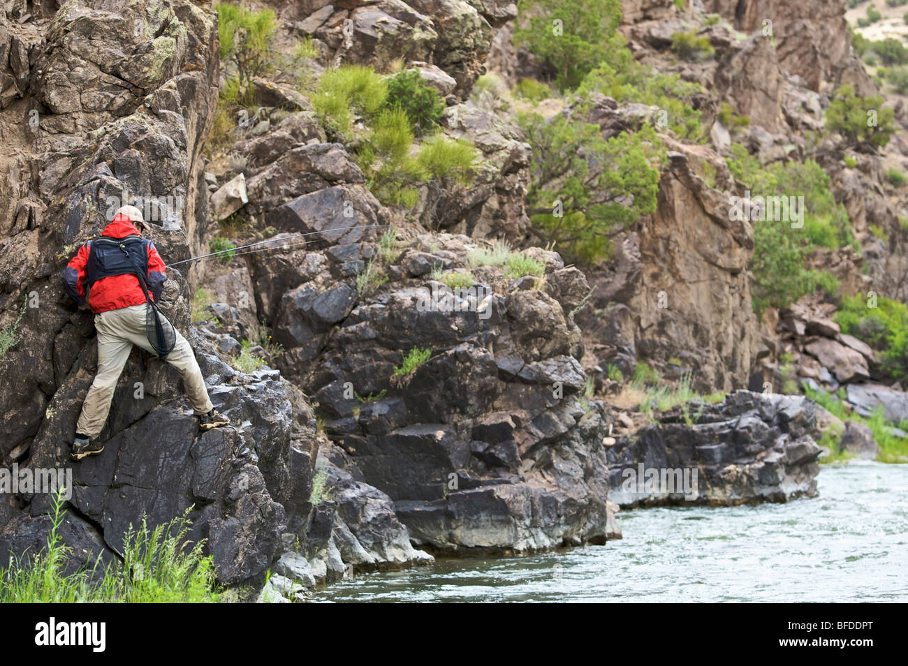 Un pescatore si arrampica su un banco roccioso per evitare di acque profonde sulle rive di un fiume. Foto Stock
