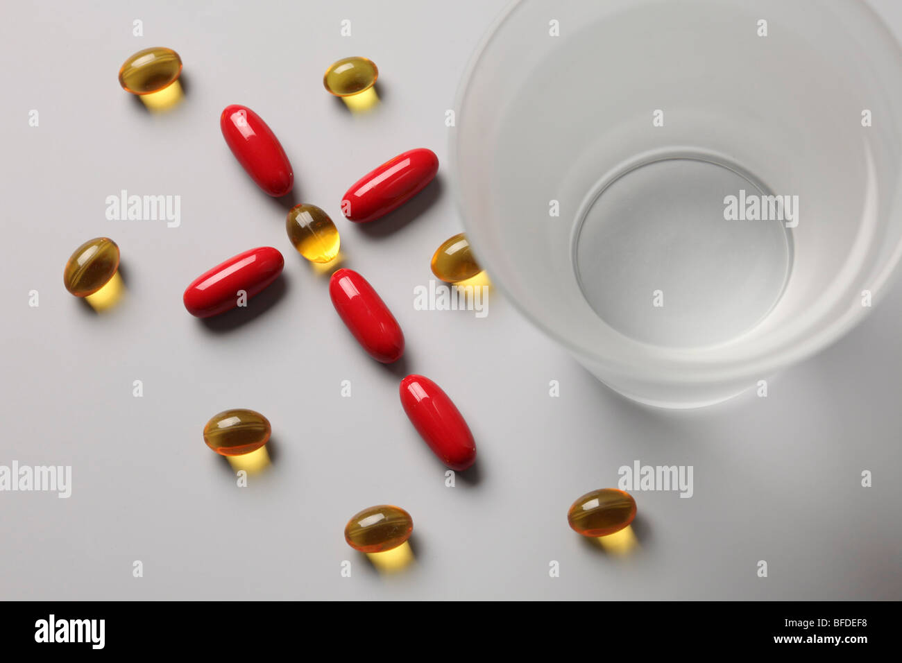 Pills formano una croce accanto a un bicchiere di acqua Foto Stock