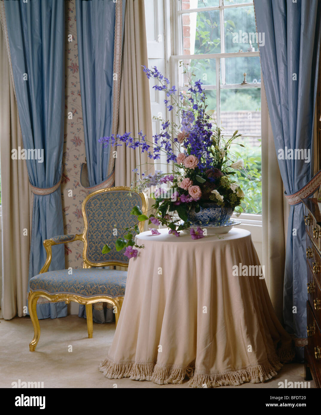 Composizioni floreali su tavola con crema di tessuto nella parte anteriore del vetro con tende blu Foto Stock