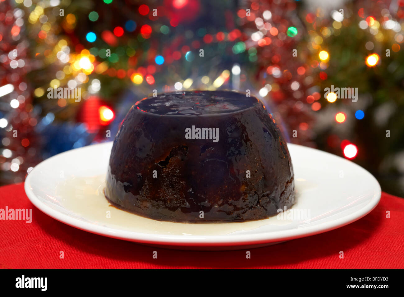 Traditional Christmas pudding impostare acceso con alcool prima di servire su un piatto nella parte anteriore di un albero di natale Foto Stock