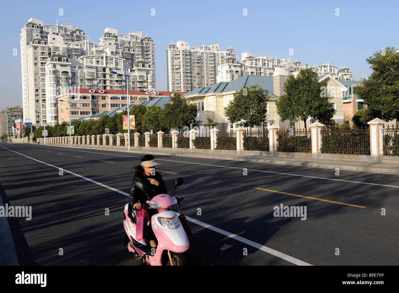 Lady riding electric motorcycle passato composto di appartamenti di lusso e ville in Songjiang nella periferia di Shanghai 2009 Foto Stock