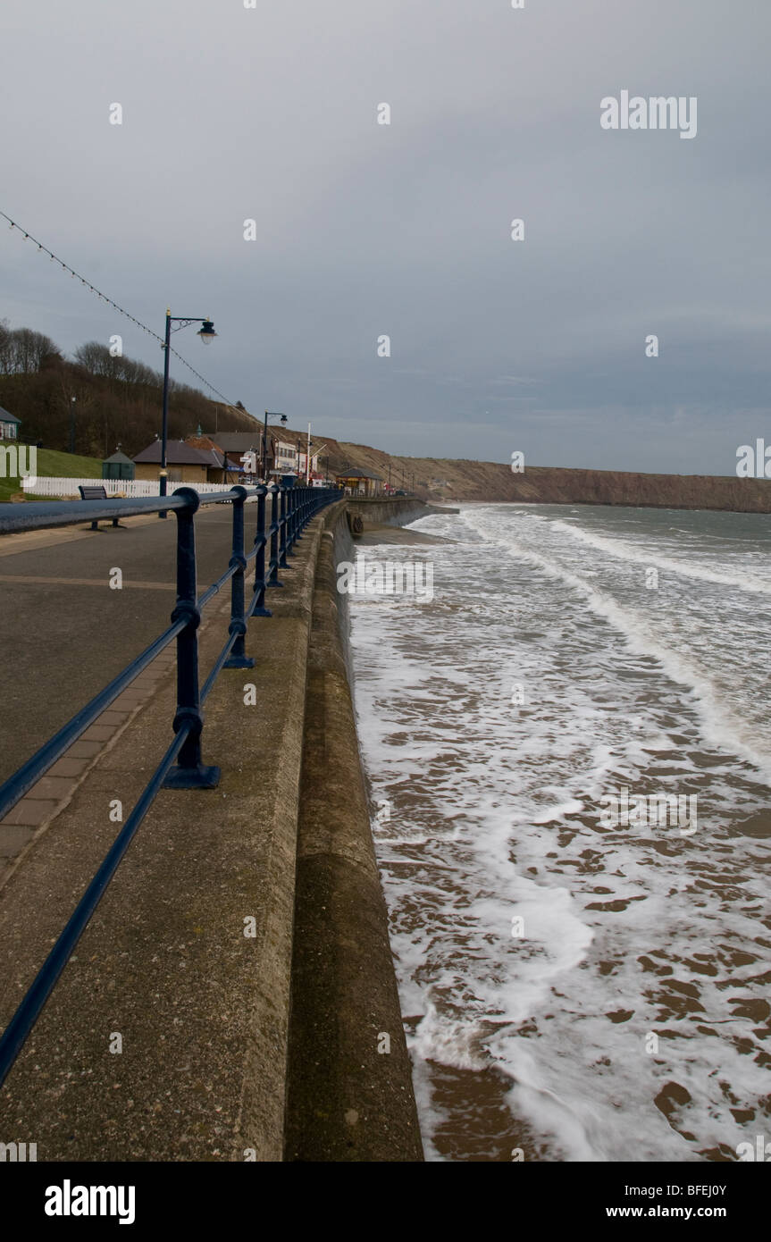 Filey promenade su un giorno ventoso. Che mostra le onde infrangersi contro le difese del mare. Foto Stock