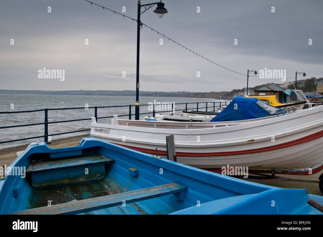 Filey promenade su un giorno ventoso. Mostra le barche da pesca tirato fuori dall'acqua e sul mare difese. Foto Stock