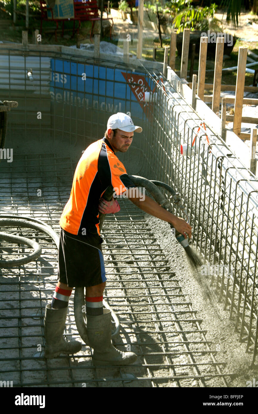 Un uomo spray di calcestruzzo nella maglia di acciaio durante la costruzione di una piscina in Australia. Foto Stock