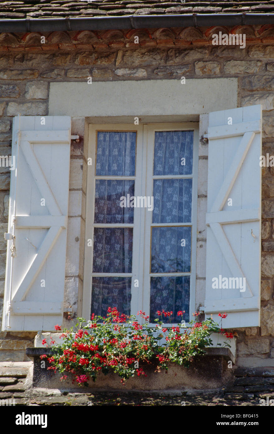 Rosso dei gerani nella finestra-box sottostante finestra di bianco con persiane di legno sulla piccola casa francese Foto Stock